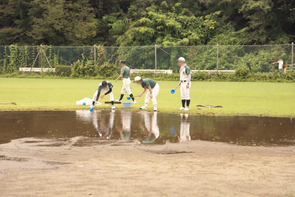 グラウンドにたまった水を取り除く指導者たち